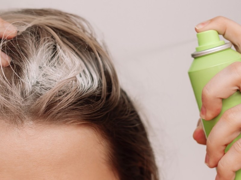 Die Nahaufnahme einer Frau, die Trockenshampoo auf ihren Haaransatz aufträgt.