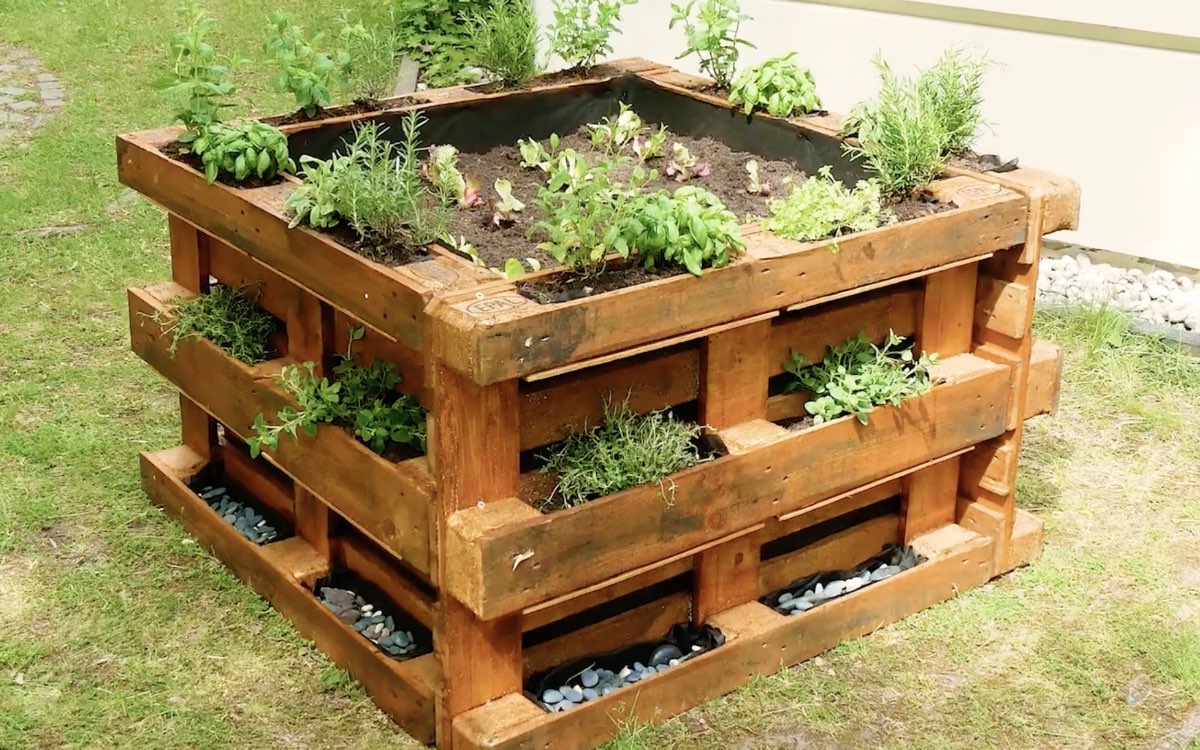 Ein Hochbeet, das aus Paletten gebaut wurde, steht in einem Garten.
