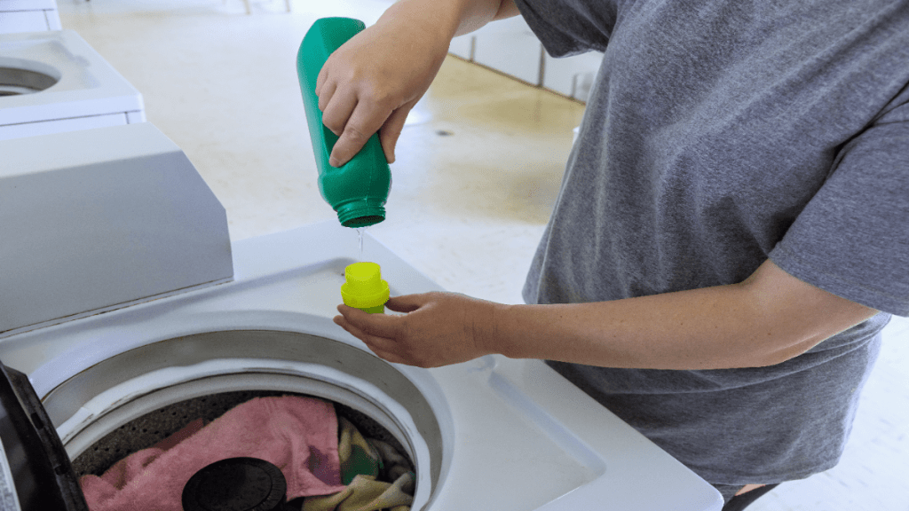 Eine Person schüttet Hygienespüler in eine Wäschetrommel.