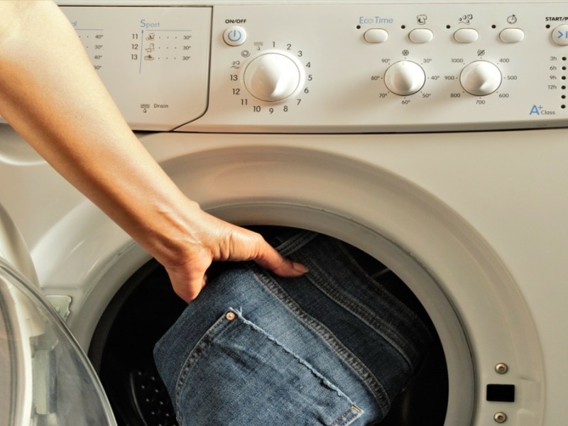 Jemand legt eine blaue Jeans in die Waschmaschine, um sie zu waschen.