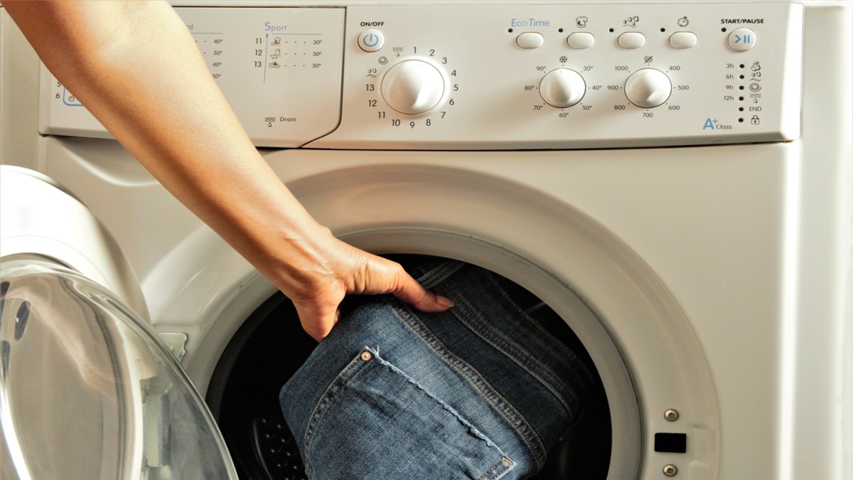 Jemand legt eine blaue Jeans in die Waschmaschine, um sie zu waschen.
