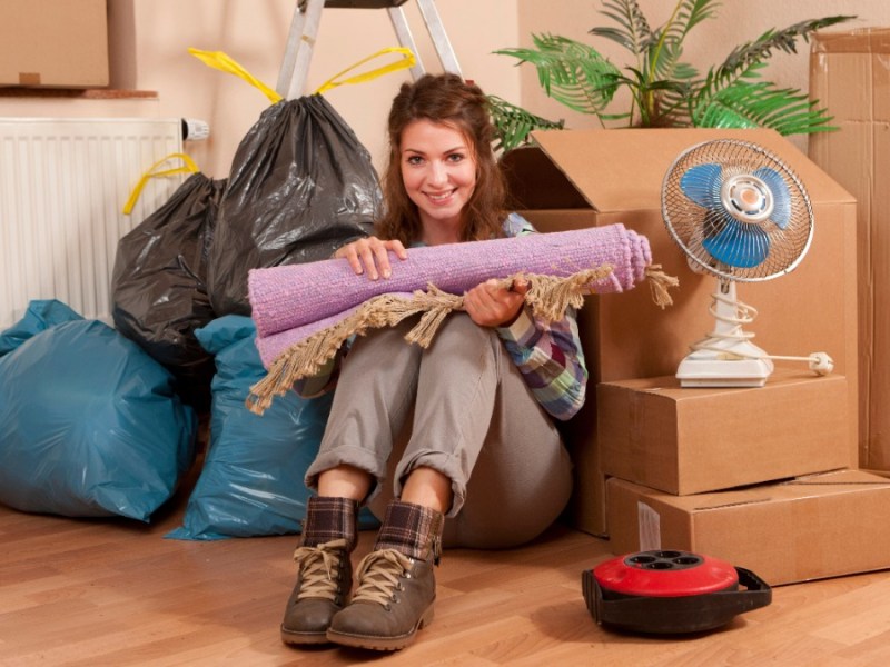 Eine Frau sitzt in ihrer ausgeräumten Wohnung zwischen Kartons und Müllsäcken.