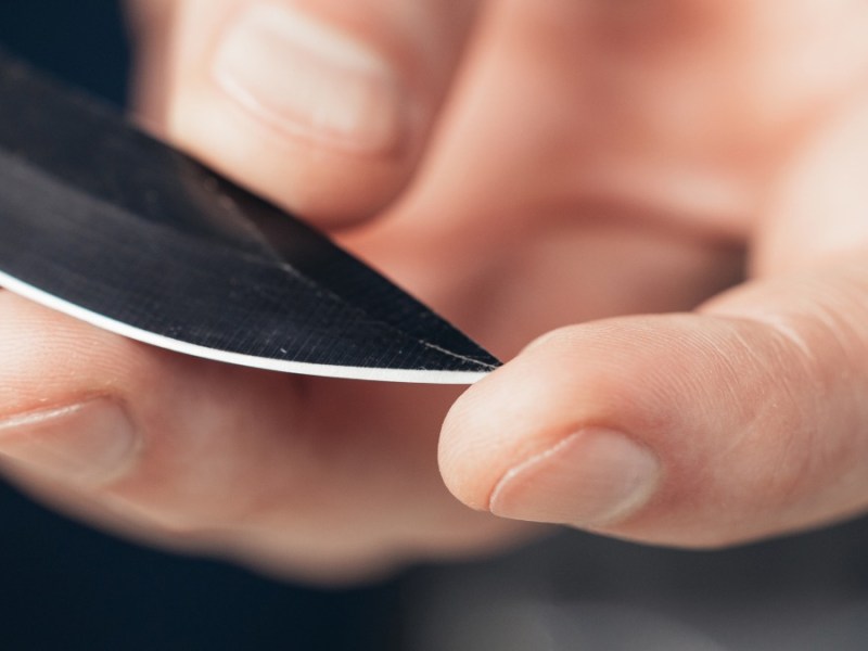 ein Messer wird in einer Hand gehalten, ein Finger drückt auf die Messerspitze