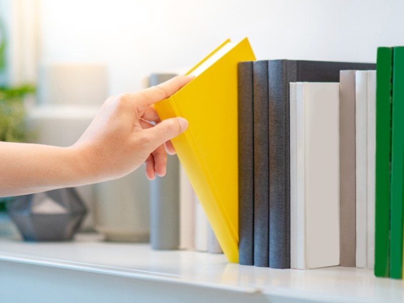 eine Hand zieht ein gelbes Buch aus dem Bücherregal