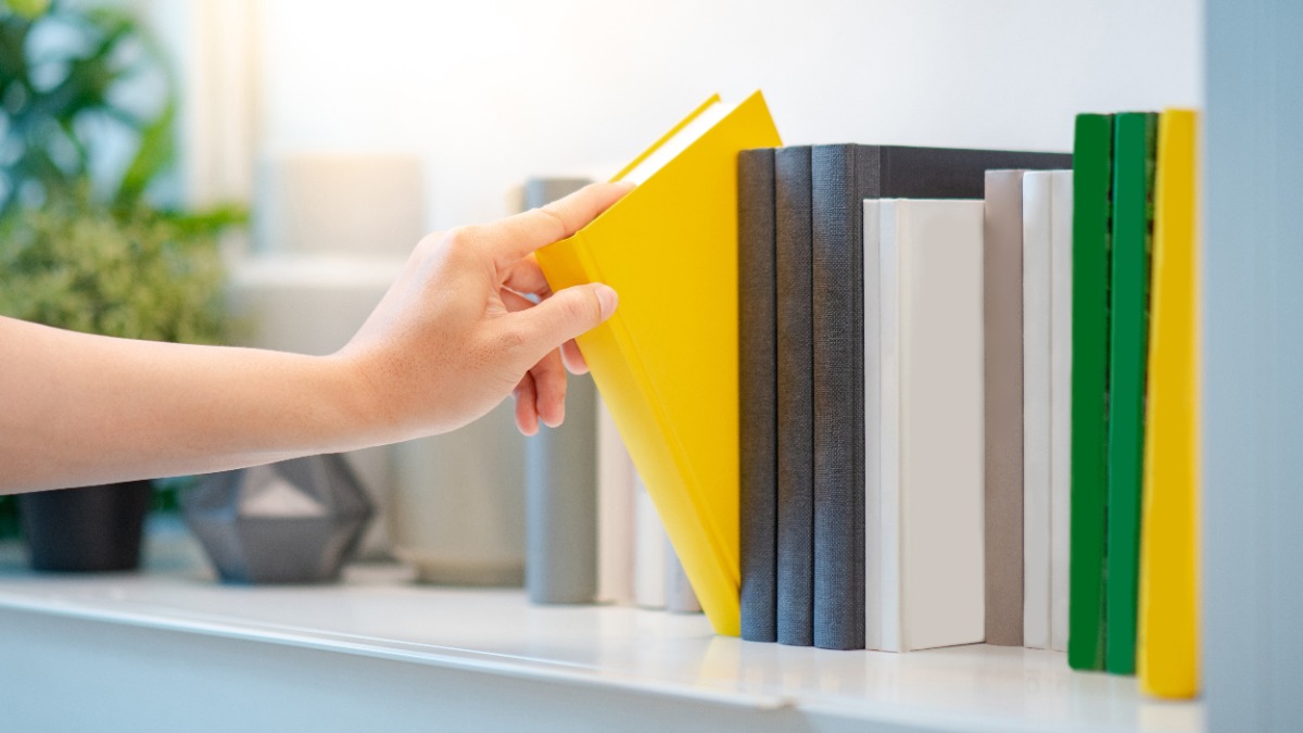 eine Hand zieht ein gelbes Buch aus dem Bücherregal