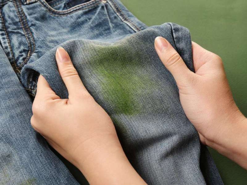 Zwei Hände halten eine Jeans mit einem grünen Grasflecken nach oben.