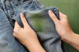 Zwei Hände halten eine Jeans mit einem grünen Grasflecken nach oben.