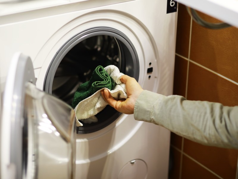 Eine Frau gibt ihre Wäsche in die Trommel einer Waschmaschine.