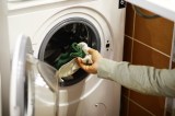 Eine Frau gibt ihre Wäsche in die Trommel einer Waschmaschine.