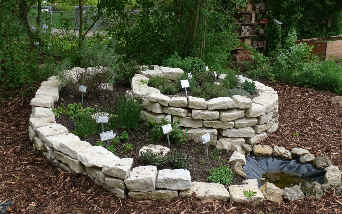 Eine mit diversen Kräutern bepflanzte Kräuterschnecke steht in einem Garten.