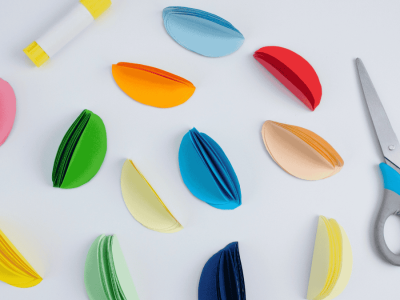 Papier-Ostereier basteln, bunte Papiereier neben Schere und Klebstoff