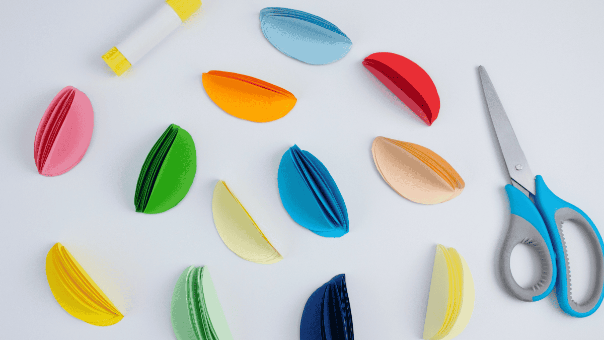 Papier-Ostereier basteln, bunte Papiereier neben Schere und Klebstoff