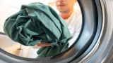 Ein Mann wirft Kleidung in eine Waschmaschine.