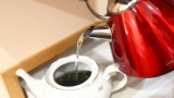 heißes Wasser wird aus einer roten Kanne in eine weiße Teekanne gegossen