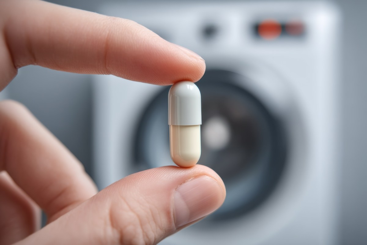 Eine Aspirin-Tablette wird vor eine Waschmaschine gehalten.