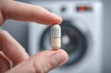Eine Aspirin-Tablette wird vor eine Waschmaschine gehalten.