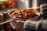 Ein Mensch stellt eine Schüssel mit Chili con Carne in den Kühlschrank.