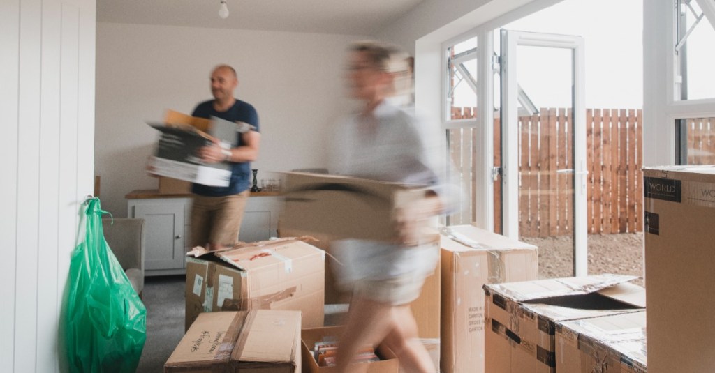 eine Frau und ein Mann tragen Umzugskartons in eine Wohnung