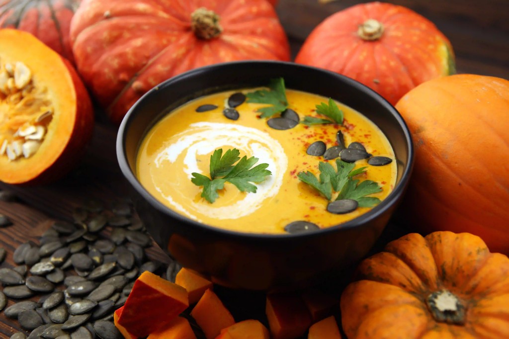 Gebratene Kürbis- und Karottensuppe mit Sahne und Kürbiskernen auf Holzuntergrund.