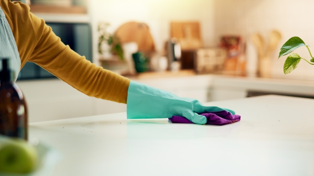 eine Frau mit Putzhandschuhen reinigt eine Küchenarbeitsplatte
