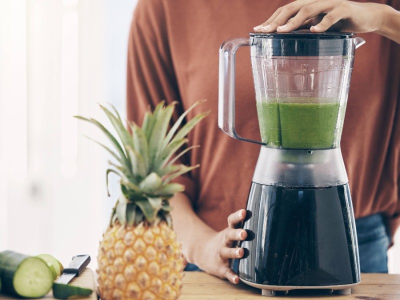 eine Frau bereitet sich einen grünen Smoothie in einem Standmixer zu