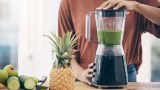 eine Frau bereitet sich einen grünen Smoothie in einem Standmixer zu