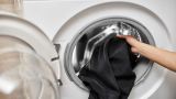 Eine Person steckt schwarze Wäsche in eine Waschmaschine.