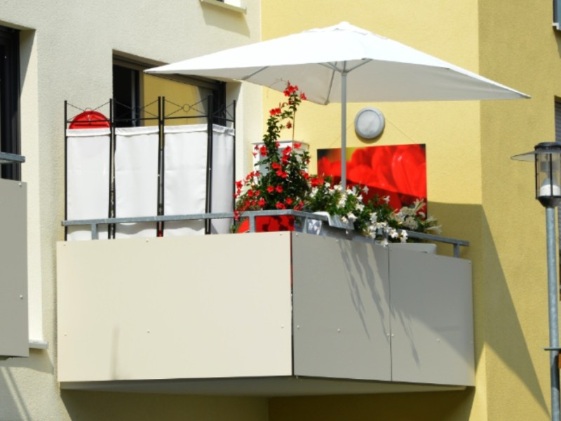 Ein Sichtschutz und ein Sonnenschirm stehen auf einem Balkon eines Wohnhauses.