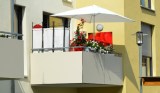 Ein Sichtschutz und ein Sonnenschirm stehen auf einem Balkon eines Wohnhauses.
