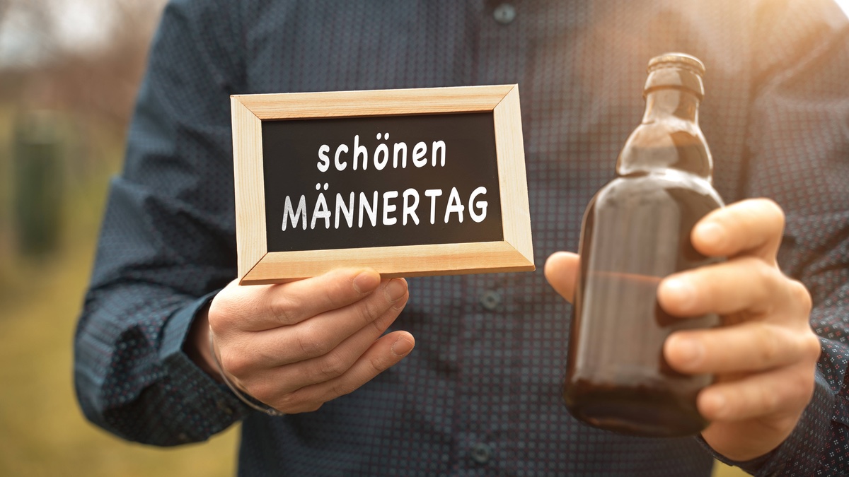 Mann mit Bier und einem Schild, auf dem steht: „Schönen Männertag“.