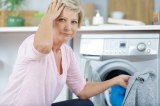 Eine Frau sitzt vor einer Waschmaschine und fasst sich an den Kopf.