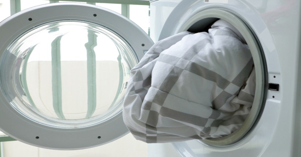 Eine Daunendecke wird in eine Waschmaschine gesteckt.