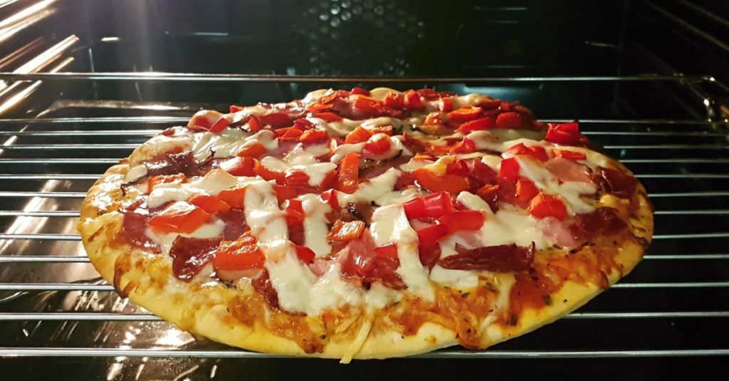 eine Pizza liegt auf dem Rost im Backofen