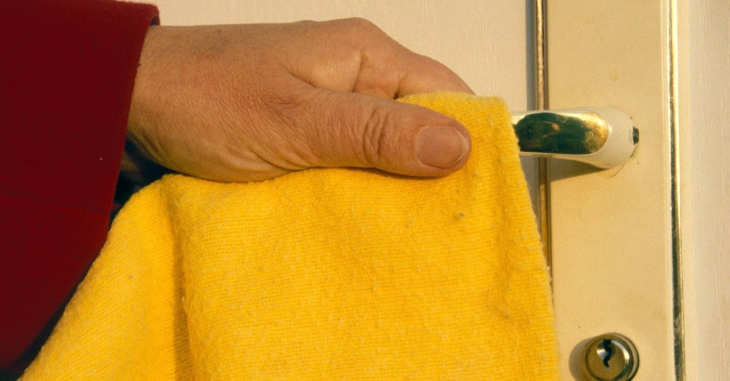 eine Türklinke wird mit einem gelben Tuch abgewischt