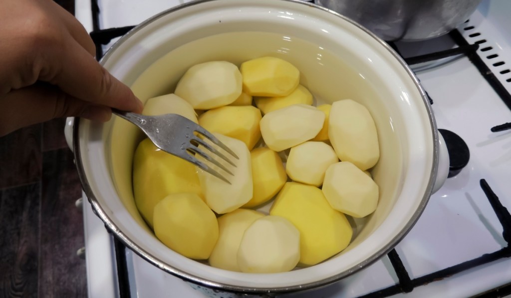 Geschälte Kartoffeln werden in einem Topf gekocht und mit einer Gabel eingestochen.