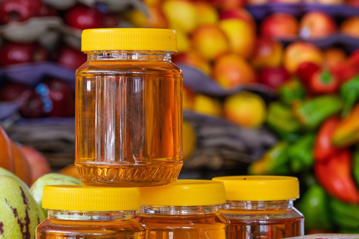 Ein Glas Honig vor einem Regal voller frischem Obst