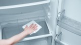 eine Hand wischt mit einem Lappen einen Kühlschrank sauber