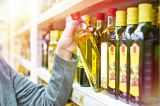 Eine Hand greift nach einer Flasche Olivenöl in einem Supermarkt.