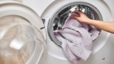 Ein Pullover wird in eine Waschmaschine gesteckt.