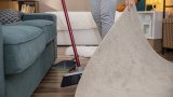 Eine Person reinigt aktiv ein Wohnzimmer, indem sie einen Teppich anhebt und den gesamten Raum aufräumt.