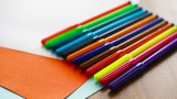 Verschiedene Filzstifte liegen neben farbigem Papier auf einem Tisch