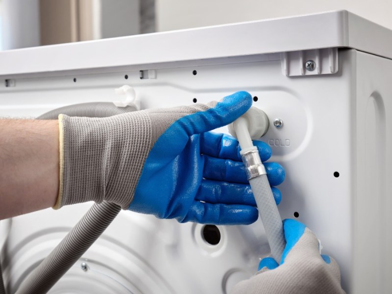 Installateur schließt Schläuche an einer Waschmaschine an
