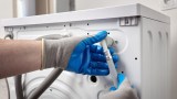 Installateur schließt Schläuche an einer Waschmaschine an