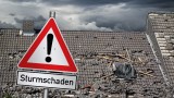 Ein Dach mit Sturmschäden im Hintergrund von einem Achtung-Verkehrszeichen mit der Aufschrift 