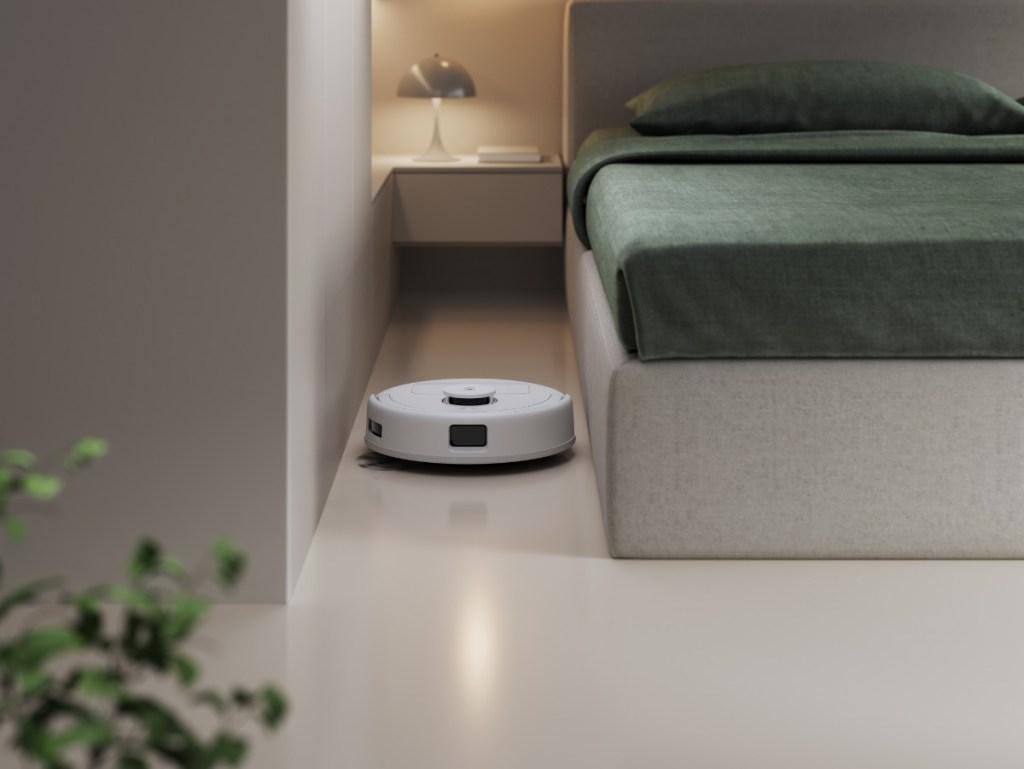 Der Deebot mini von Ecovacs neben einem Bett.