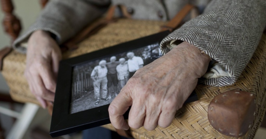 eine Seniorin hält ein Foto und einen Koffer in den Händen