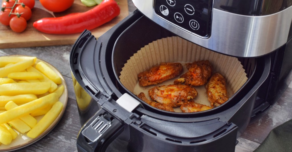 in einer Heißluftfritteuse befinden sich Chicken-Wings auf Backpapier