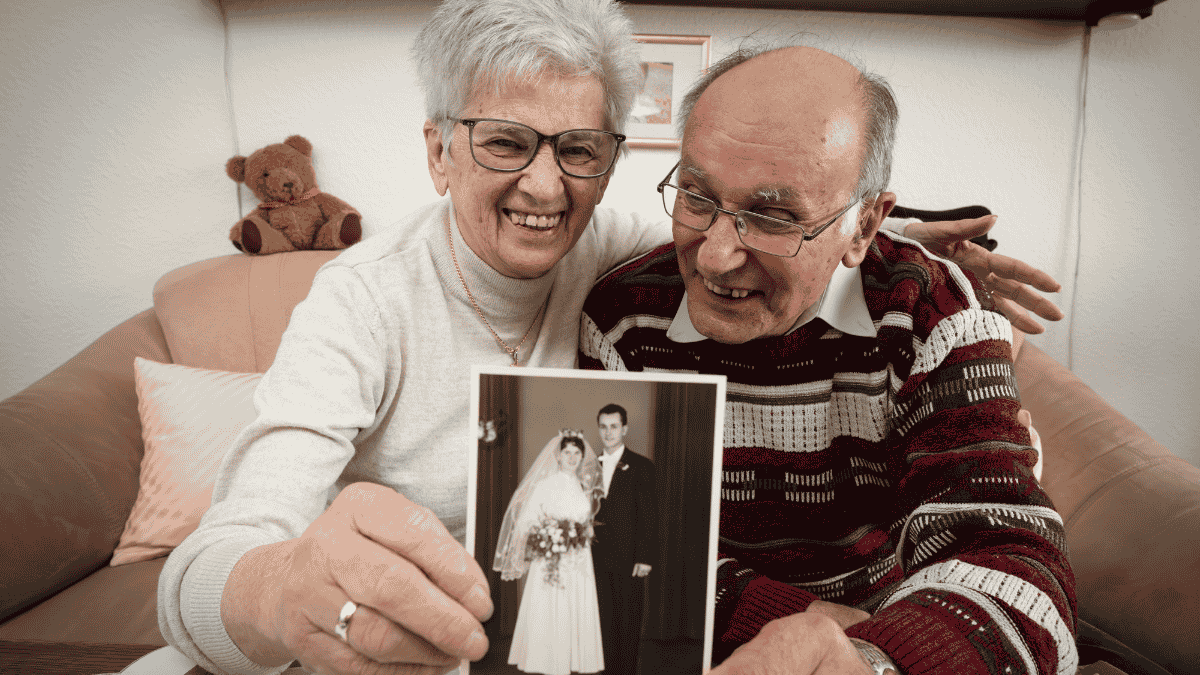 Hochzeitstage Namen, Älteres Ehepaar hält Hochzeitsfoto in die Kamera