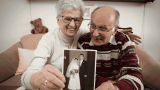Hochzeitstage Namen, Älteres Ehepaar hält Hochzeitsfoto in die Kamera