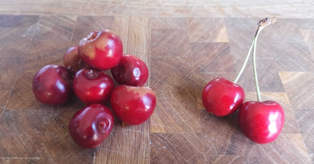 verschimmelte Kirschen ohne Stiel und zwei frische Kirschen mit Stiel liegen auf einem Holzbrett